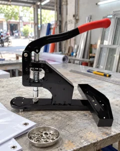Máy dập khuy bạt 10 mm cối hoa sen BEDO tại bàn làm việc trong xưởng quảng cáo.