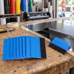 Gạt decal lưỡi nỉ trên bàn xưởng cạnh tấm vật liệu và decal đen
